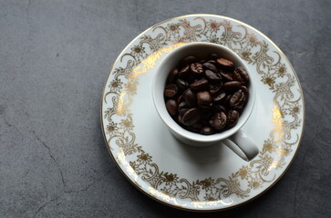 Close-up view of coffee beans placed inside a vintage porcelain cup, set on a rustic burlap background.