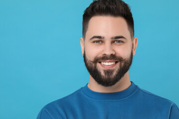 Portrait of happy young man with mustache on light blue background. Space for text