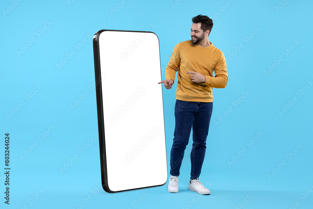 Aufkleber man pointing at huge mobile phone with empty screen on light blue background. mockup for design