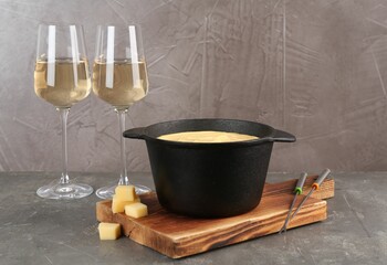Fondue pot with tasty melted cheese, forks and wine on grey table