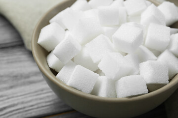 White sugar cubes in bowl on wooden table, closeup