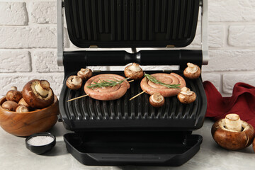 Electric grill with homemade sausages, rosemary and mushrooms on marble table