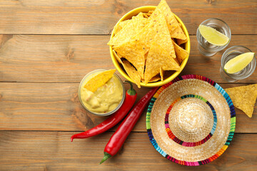 Mexican sombrero hat, tequila, chili peppers, nachos chips and guacamole on wooden table, flat lay....