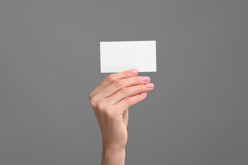 Woman holding blank business card on grey background, closeup. Space for text