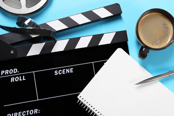 Movie clapper, film reel, coffee, notebook and pen on light blue background, flat lay