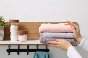 Woman stacking clean towels on shelf indoors, closeup