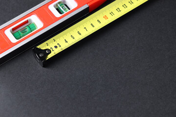 Building level and tape measure on dark background. Space for text