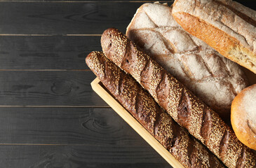 Basket with different types of fresh bread on black wooden table, top view. Space for text - obrazy, fototapety, plakaty