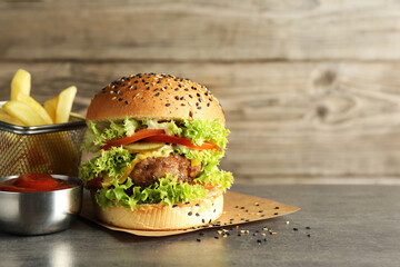 Burger with delicious patty, french fries and sauce on gray table, space for text