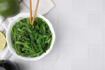 Tasty seaweed salad served in bowl on white tiled table, flat lay. Space for text