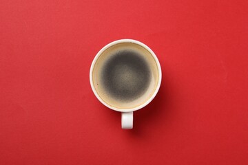 Aromatic coffee in cup on red background, top view