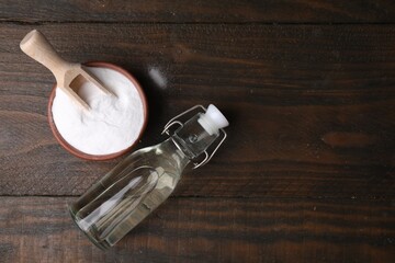 Vinegar in glass bottle and baking soda on wooden table, top view. Space for text