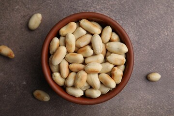 Roasted peanuts in bowl on brown table, top view