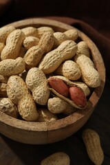 Fresh unpeeled peanuts in bowl on wooden table, closeup