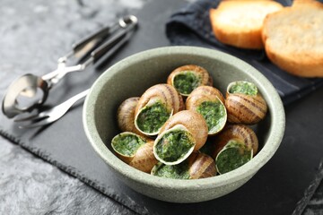 Delicious cooked snails served on grey textured table, closeup