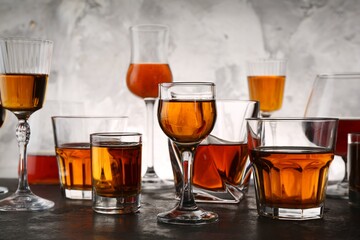 Different delicious liqueurs in glasses on grey table