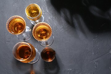 Many different liqueurs in glasses on dark textured table, flat lay. Space for text