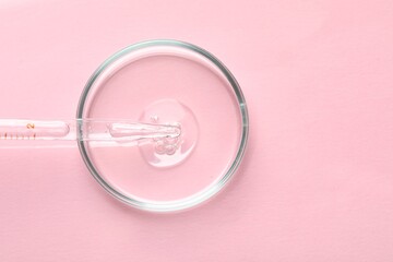 Glass pipette and petri dish with liquid on pink background, top view. Space for text