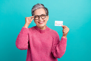 Photo of smart cheerful person dressed knitwear sweater touch glasses demonstrate debit card in arm isolated on teal color background