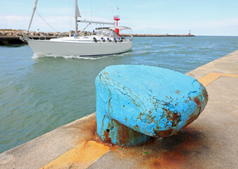 blue bollard for mooring ships to the dock of the port and a fast ship sailing away