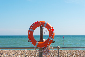 lifebouy, orange lifebouy by a beach and sea with blue sky
