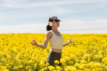 Sporty woman enjoying sunshine in a yellow field, medititating and getting away from it all wearing...