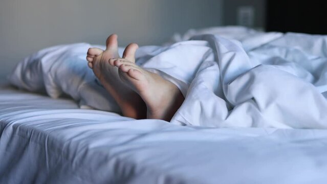 A close-up of the legs of a sleeping small child on a large white bed, embodying the concept of sleep and rest