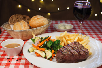 Restaurant grilled piece of steak sprinkled with pepper, french fries and vegetables, grapes and bread