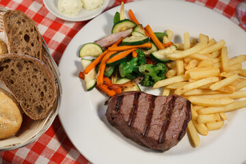 Restaurant grilled piece of steak sprinkled with pepper, french fries, vegetables and bread