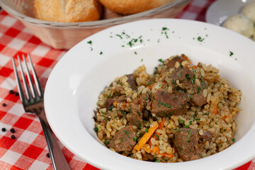 Georgian pilaf with pieces of meat in a white plate on the kitchen table close-up