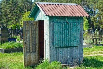 wooden with green boards, public, homemade, primitive, with a roof and an open door, the toilet...