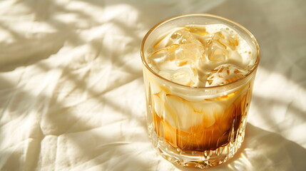 Coffee latte ice with milk, caramel syrup and ice cubes in a transparent glass glass, on a white table with sun rays from the window, close-up, top view in the corner