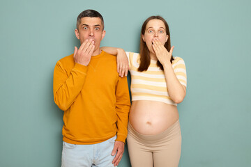 Shocked family waiting baby isolated over blue background wife and husband looking at camera with...