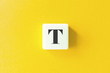 Capital Letter T. Text on Block Letter Tiles against Yellow Background.