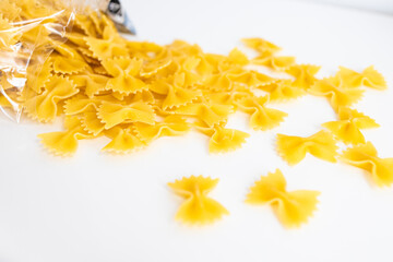 Heap of dry eggless farfalle pasta isolated on a white background. Closeup of spilled yellow...