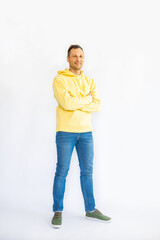 Full length young smiling cheerful man in his 20s wearing yellow hoodie , holding his arms crossed in a folded position, looking at the camera, isolated on a white background. Studio portrait