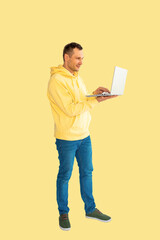 Young Caucasian man wear yellow hoodie and jeans using laptop touch screen. Full body isolated on yellow background.