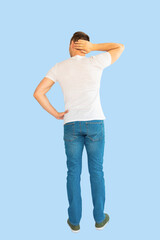 Full length back view of young man looking thoughtful while holding his head, isolated on blue background.