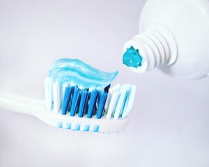 Applying toothpaste to a brush on a light background, close-up. Blue brush with emerald toothpaste, concept of oral cleanliness and health. Teeth and dentistry.