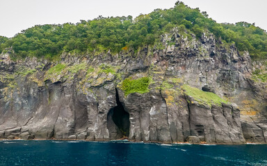 A typical banded zoning of volcanic rocks, i.e. massive rocks with regular columnar joints underlying fractured polyhedral rocks,  around a large sea cave near Yunohana Falls in Shiretoko, Hokkaido.