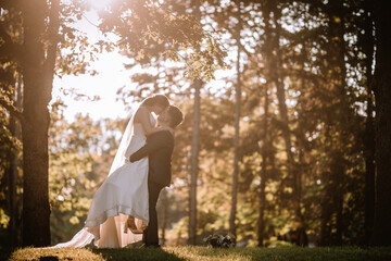 Valmiera, Latvia - August 19, 2023 - Bride and groom share a kiss in a sunlit forest, with the...