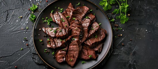 Sliced beef liver grilled and served on a plate with a black stone backdrop. Viewed from above in a flat lay style.