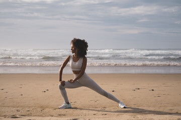 Fit black woman doing legs stretching exercise at the beach. Healthy and fitness lifestyle. Outdoor...