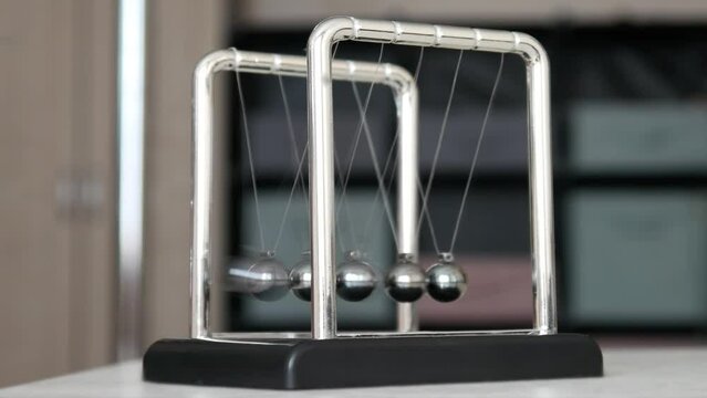 A Newton's cradle on the table close-up and a child's fingers pulling back one sphere and releasing it starting the pendulum