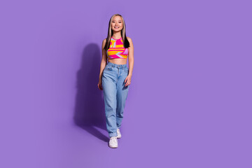 Fototapeta premium Full length photo of adorable cheerful girl wear stylish clothes walk empty space isolated on purple color background