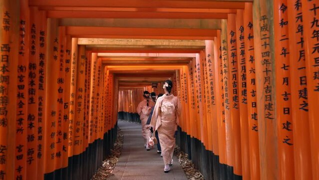 Women in traditional Japanese kimonos walk through the red torii gates at Fushimi Inari shrine in Kyoto, Japan, slow motion shot.	
