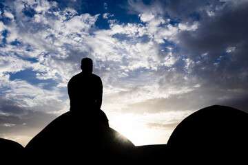 backlit shot of isolated man sitting at wall watching sunset with dramatic sky at dusk