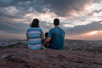 isolate couple with infant watching city landscape at mountain top with dramatic sky at dusk