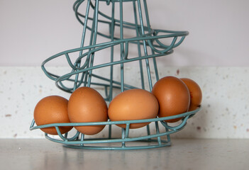 Brown eggs in a turquoise wire spiral basket on a kitchen counter with a white textured background