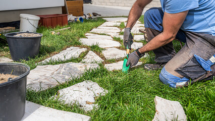 Gardening. A man makes a footpath in the grass from travertine rustic stone.